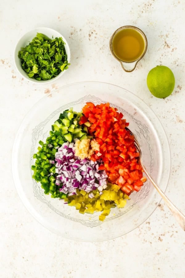 Calling all pickle lovers! This tangy Pickle de Gallo recipe is a game-changing condiment that adds a fresh, tangy twist to any meal. Fresh ingredients are placed in a glass mixing bowl.
