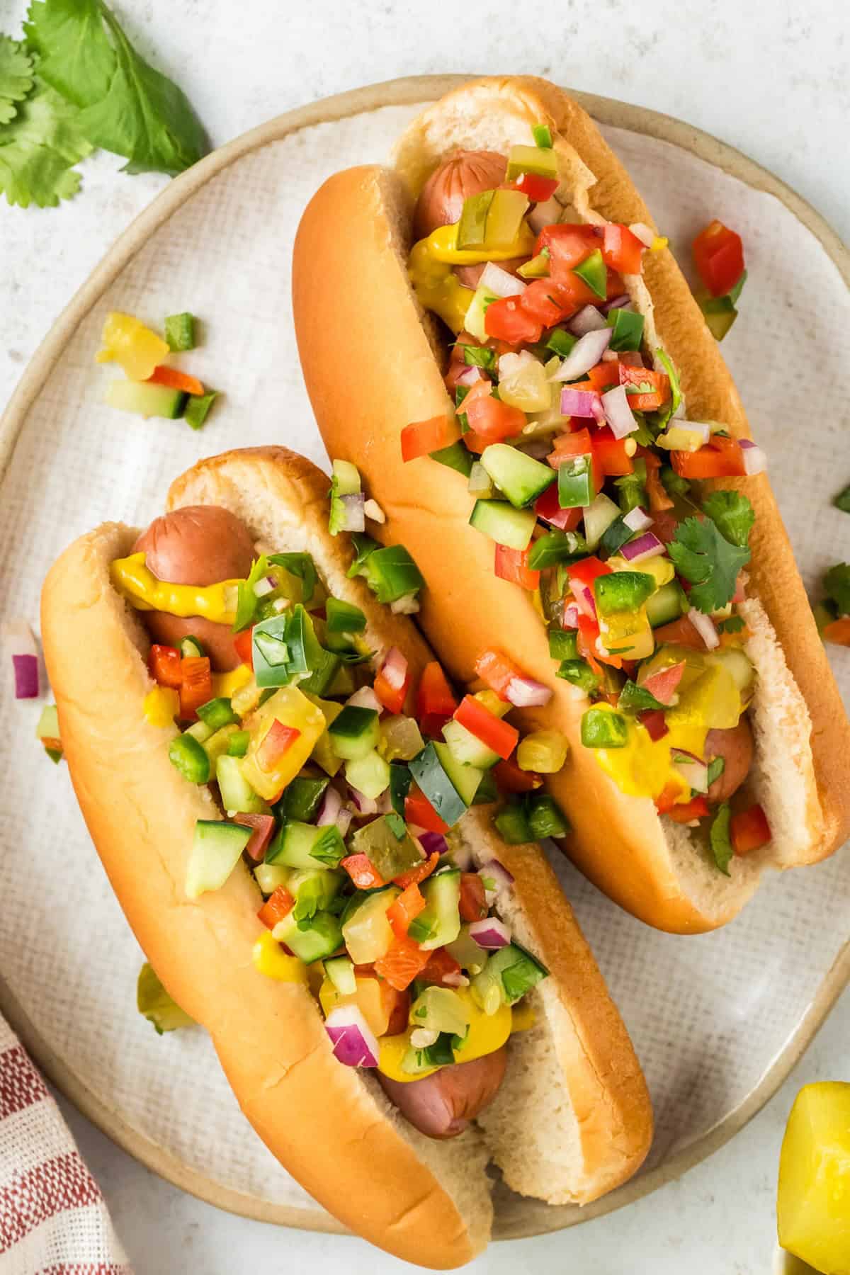 Calling all pickle lovers! This tangy Pickle de Gallo recipe is a game-changing condiment that adds a fresh, tangy twist to any meal. Pickle de gallo is garnishing two hot dogs on a white plate.