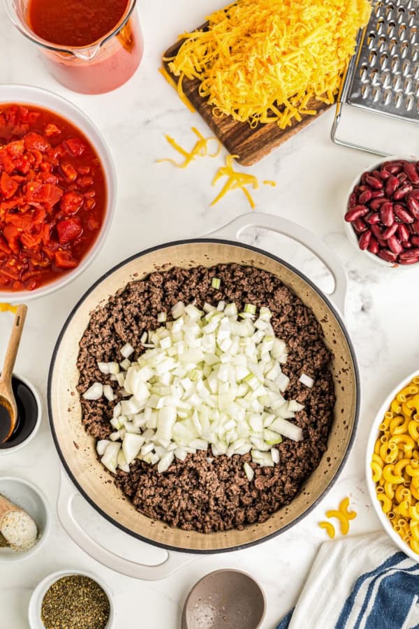 Chopped onions are placed on top of cooked ground beef in a pot.