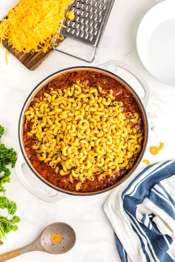 Uncooked macaroni noodles mixed into a large white pot.