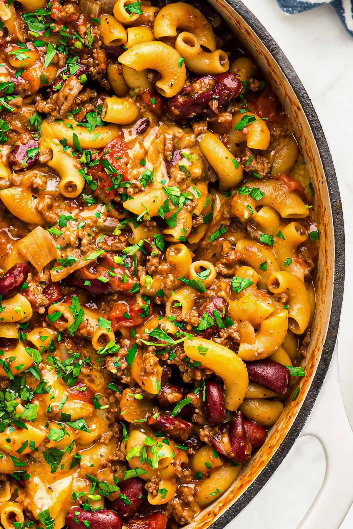 This easy, one-pot Beef Goulash recipe is comfort food at its best with cheesy ground beef and tender noodles in a robust tomato sauce. Fresh green herbs are sprinkled across the top of a pot of American-style beef goulash.