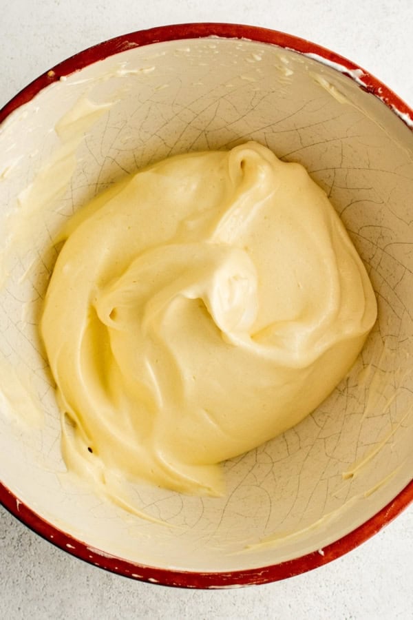 Bowl of creamy pancake batter with a smooth, thick texture in a red-rimmed ceramic bowl on a light countertop.