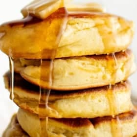 A stack of fluffy Japanese soufflé pancakes topped with melting butter and drizzled with syrup.