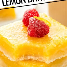 Close-up of two thick lemon bars stacked on a plate with a bite taken out of the top bar, topped with raspberries and lemon zest.