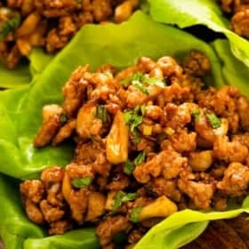 Close-up of chicken lettuce wraps filled with seasoned minced chicken, mushrooms, and chopped herbs, served on a wooden board.