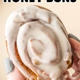 A hand holding a homemade honey bun covered in white icing.