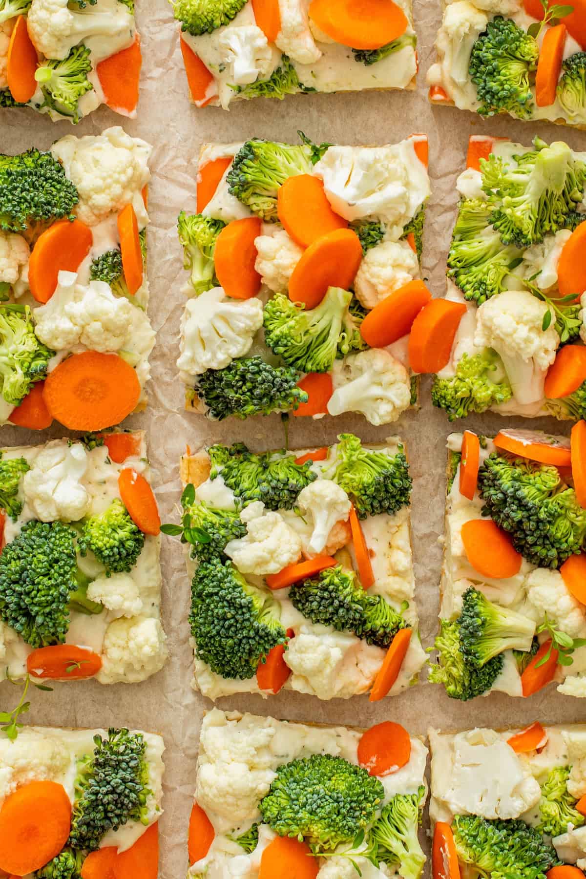 Rectangular crescent roll veggie pizza slices topped with fresh broccoli, cauliflower, and carrot rounds are arranged on a sheet of parchment paper.