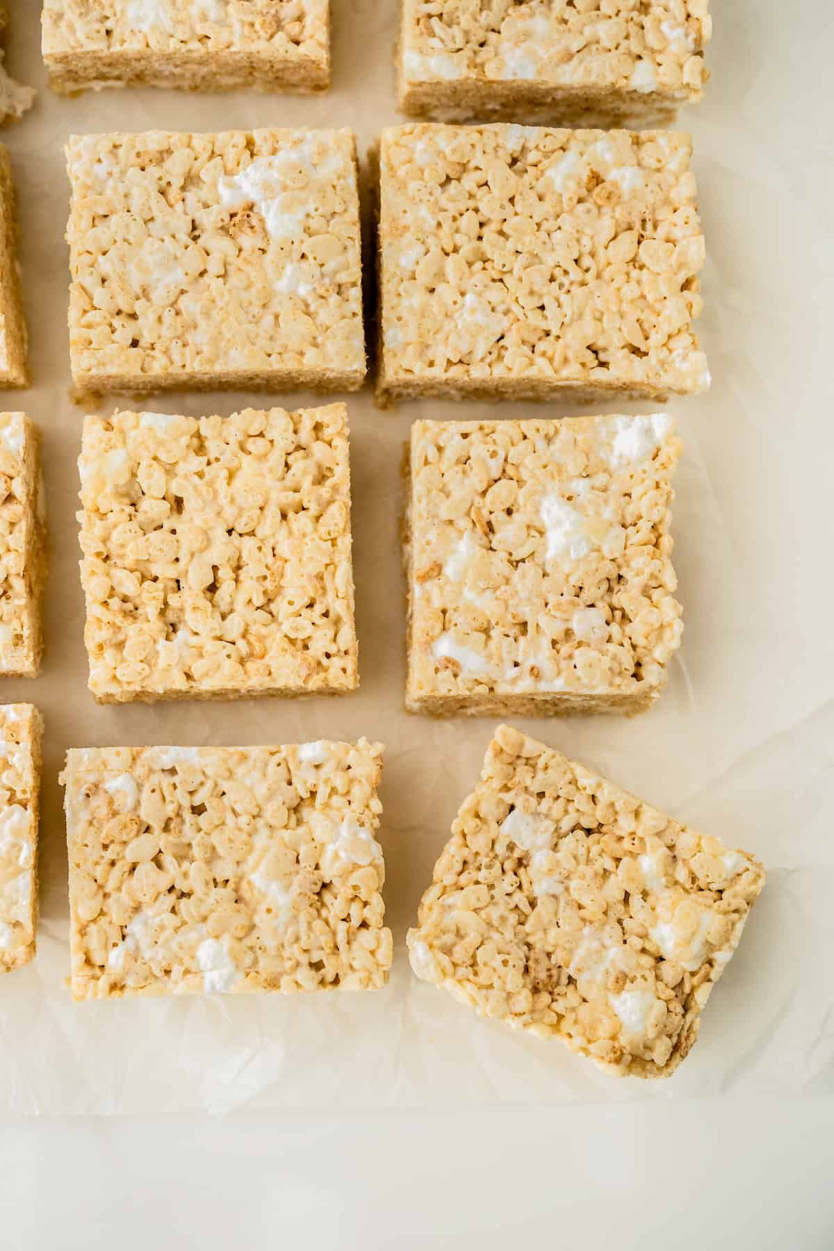 Close-up of several homemade brown butter rice krispie treats cut into squares and arranged on parchment paper.