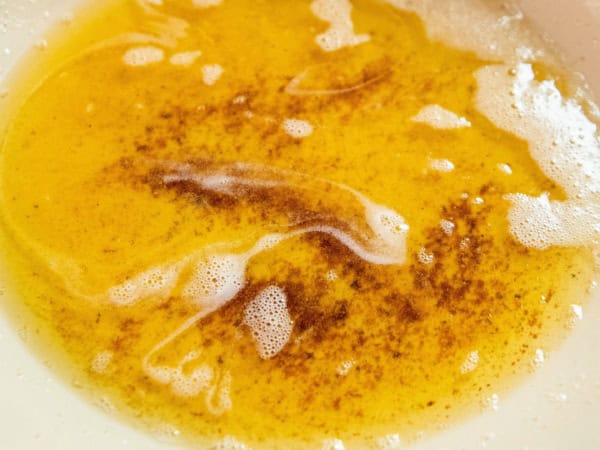 Melted brown butter with brown specks and foam in a pan, showing a golden color and a slightly frothy texture on the surface.