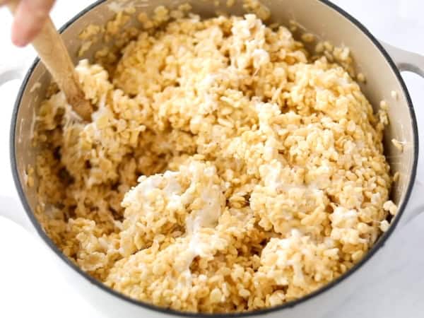 A close-up of a large pot filled with Rice Krispies cereal and melted marshmallows being stirred with a wooden spoon.