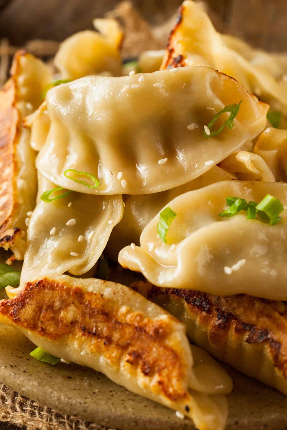 Make your favorite take out food at home with this easy Chinese Dumplings recipe in under an hour! They are crispy, juicy, and full of flavor! A close-up of freshly cooked Chinese dumplings garnished with chopped green onions and sesame seeds, showing a mix of crispy golden-brown and soft, steamed textures.