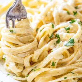 Close-up of creamy fettuccine Alfredo pasta, garnished with chopped parsley, being twirled around a fork.