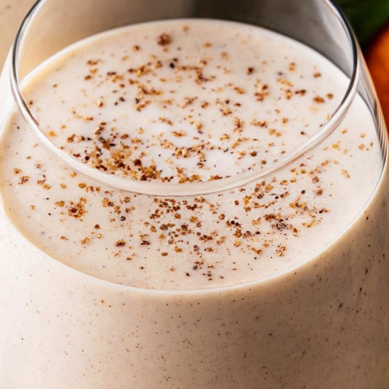 A close-up of a creamy glass of Coquito, topped with a sprinkle of ground nutmeg.