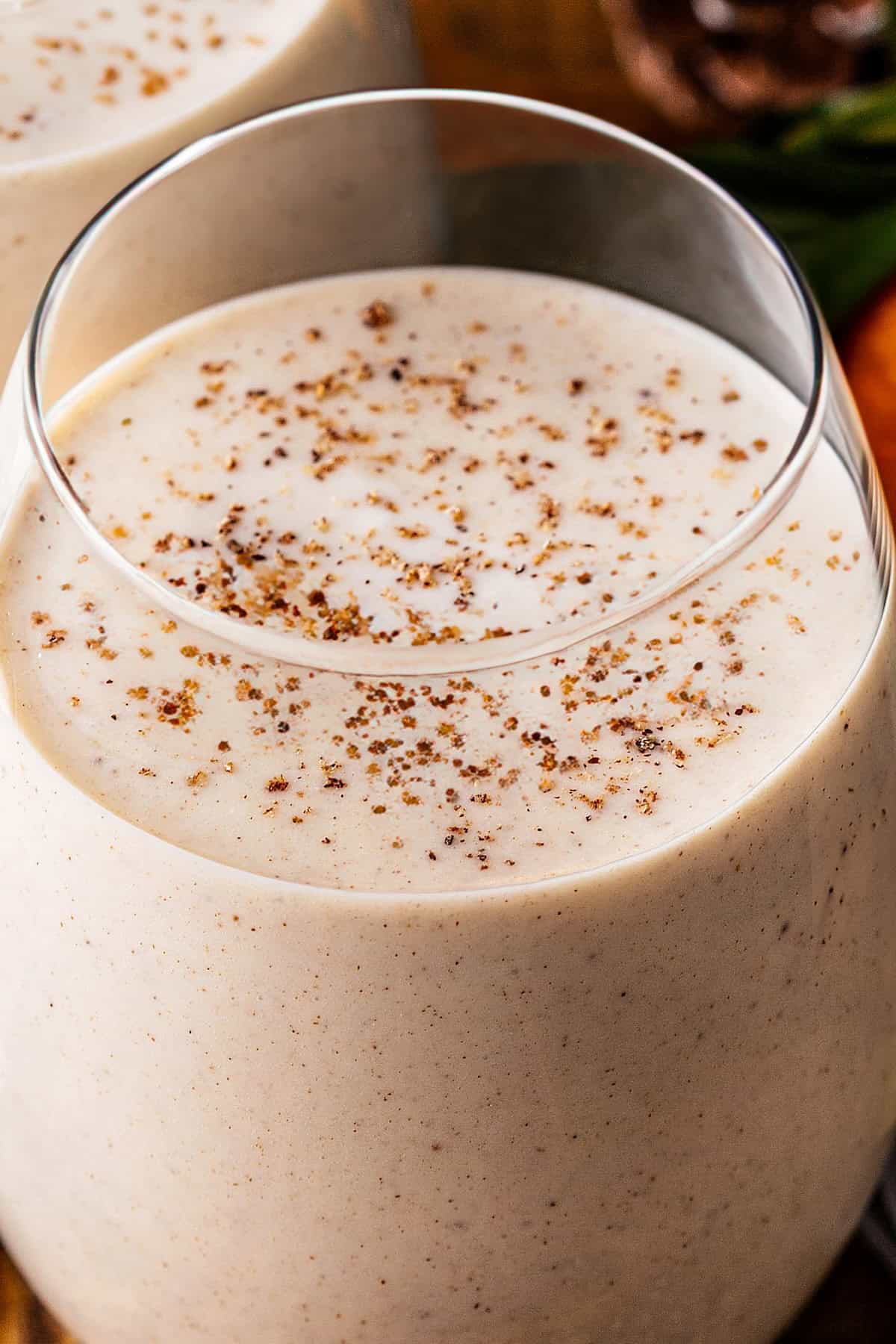 A close-up of a creamy glass of Coquito, topped with a sprinkle of ground nutmeg.