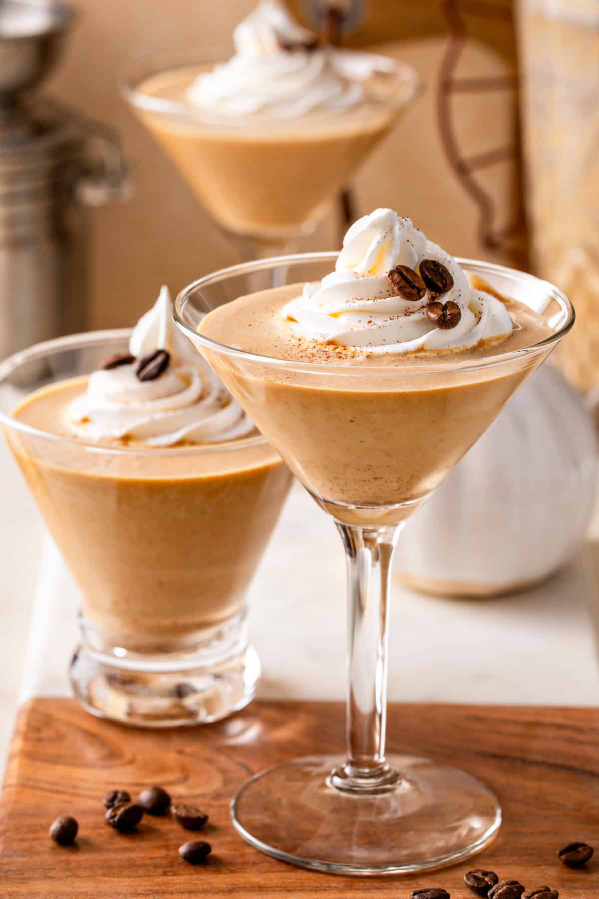 Three pumpkin spice espresso martini glasses are garnished with whipped cream, pumpkin spice, and coffee beans.