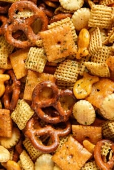A close-up of a homemade chex mix featuring pretzels, cheese crackers, oyster crackers, goldfish crackers, and square cereal pieces, all coated with seasoning.