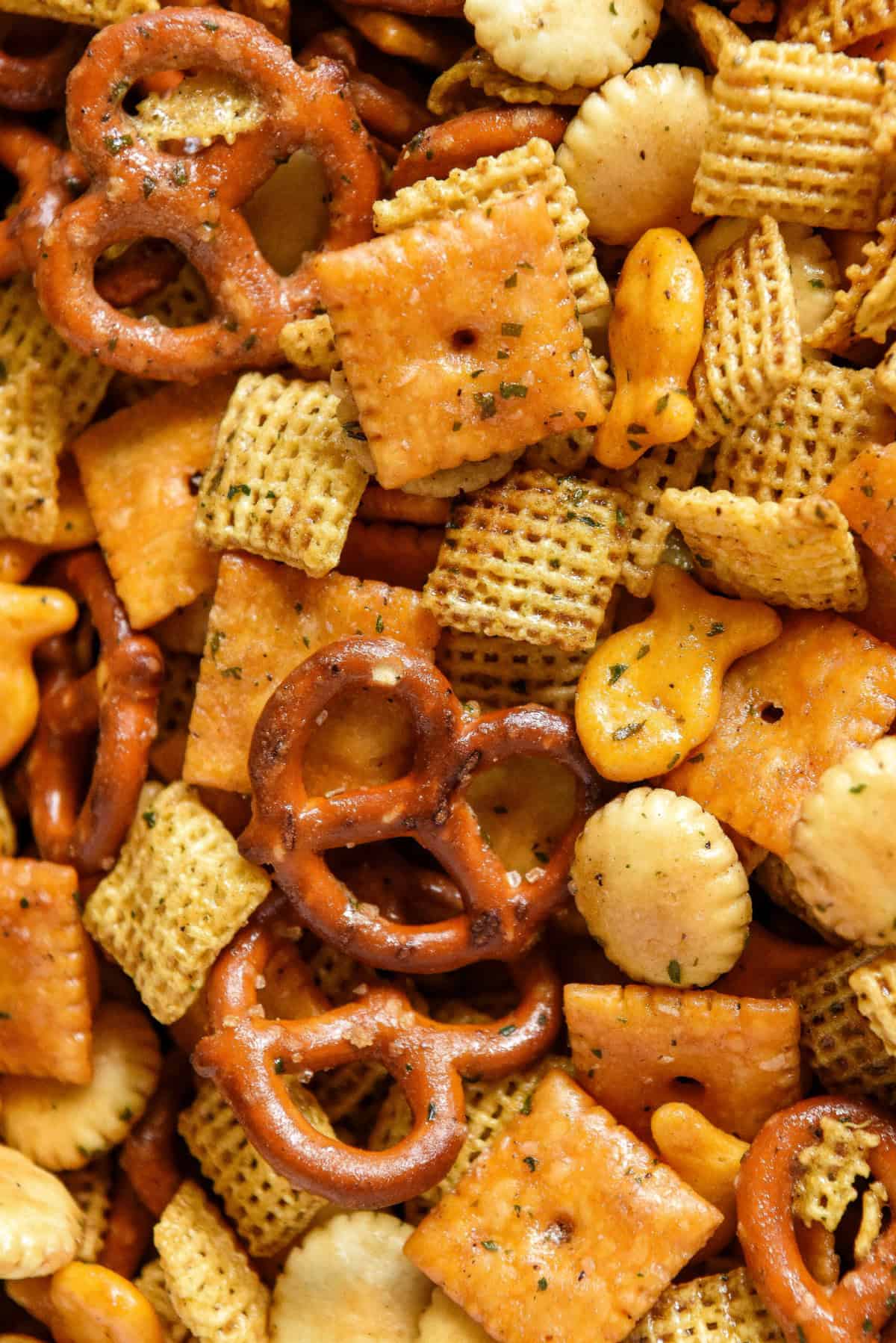 A close-up of a homemade chex mix featuring pretzels, cheese crackers, oyster crackers, goldfish crackers, and square cereal pieces, all coated with seasoning.