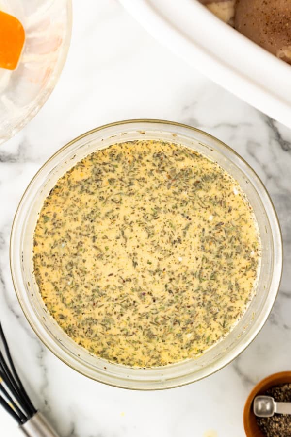 A glass bowl filled with a mixture of seasonings, dry milk powder, water and chicken bouillon sits on a marble countertop.