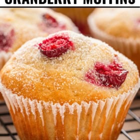 Close-up of a golden cranberry muffin topped with sugar and cranberry pieces, resting on a cooling rack.