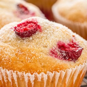 Close-up of a homemade cranberry muffin topped with sugar and cranberries, placed on a cooling rack.
