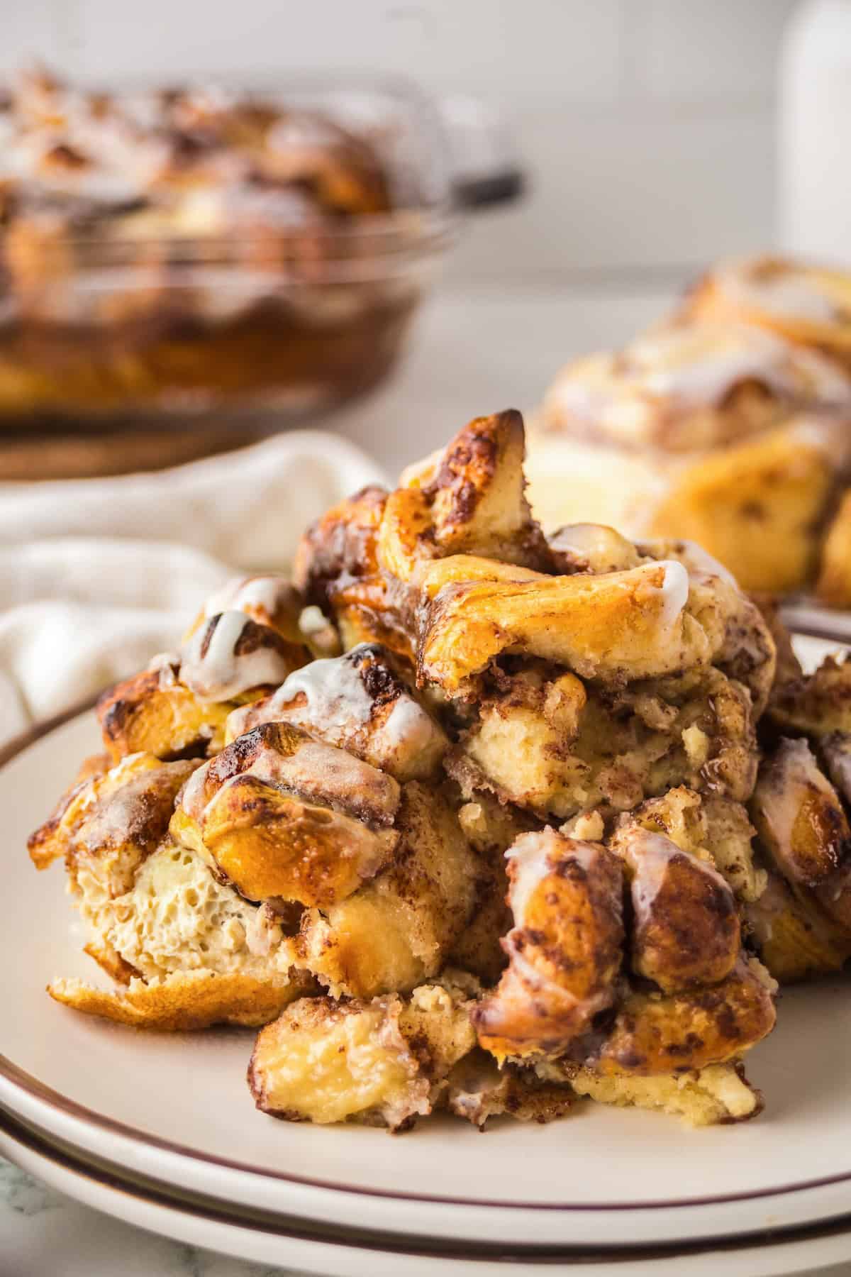 Make easy with just 6-ingredients, every bite of this Cinnamon Roll Casserole tastes like the gooey and warm center of a cinnamon roll! A plate piled with a serving of gooey cinnamon roll casserole drizzled with white icing.