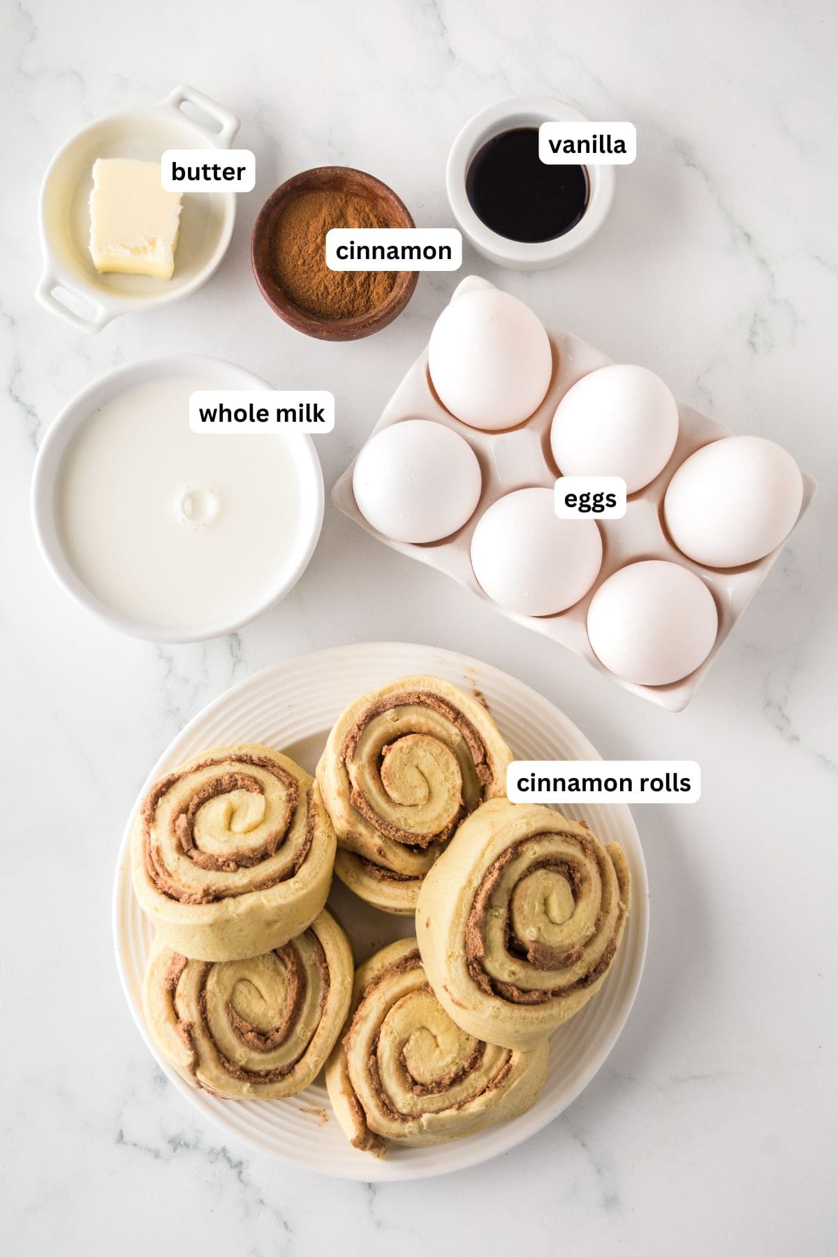 Make easy with just 6-ingredients, every bite of this Cinnamon Roll Casserole tastes like the gooey and warm center of a cinnamon roll! A flat lay of cinnamon roll casserole recipe ingredients on a white surface: butter, cinnamon, vanilla, whole milk, eggs in a carton, and six cinnamon rolls on a plate.