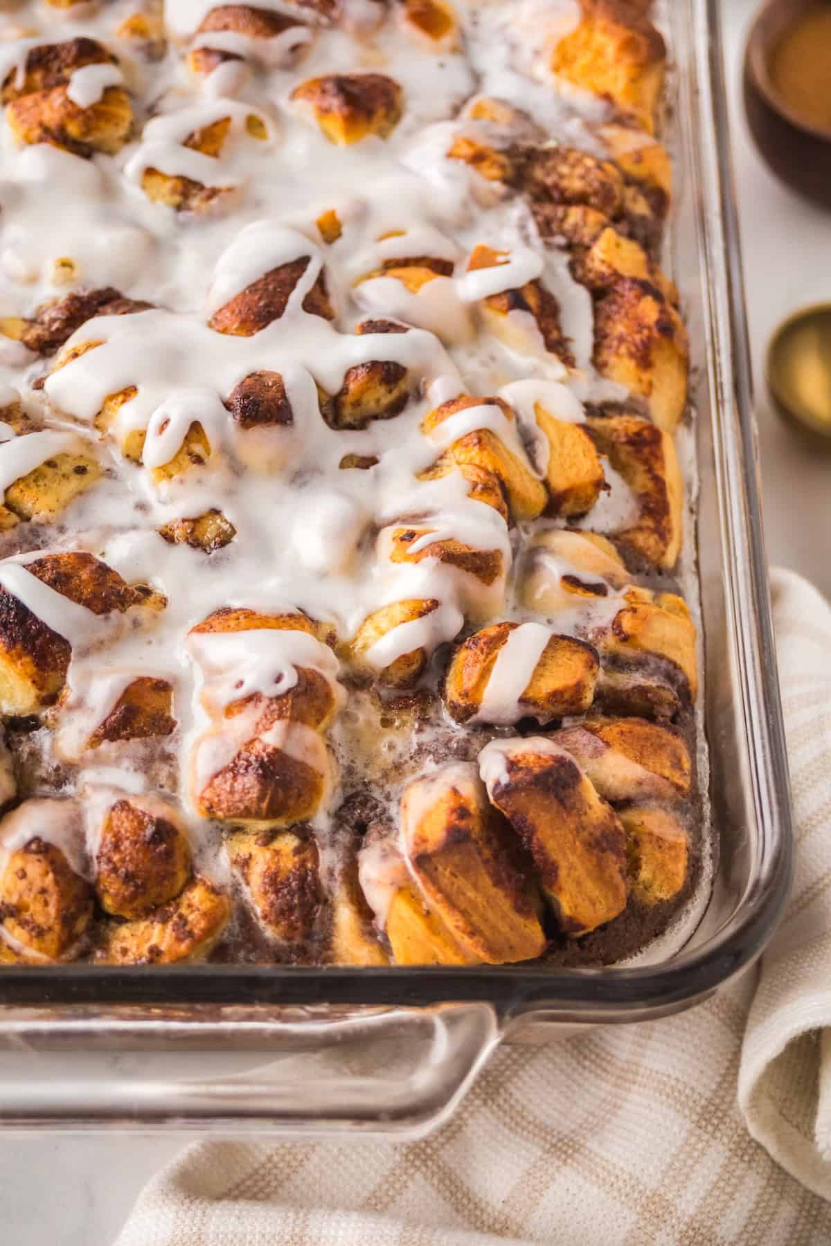 Make easy with just 6-ingredients, every bite of this Cinnamon Roll Casserole tastes like the gooey and warm center of a cinnamon roll! A glass baking dish filled with golden-brown cinnamon roll casserole topped with white icing.