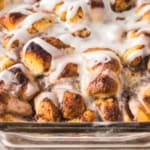 Close-up of a glass baking dish filled with golden-brown cinnamon roll casserole topped with a white icing drizzle.
