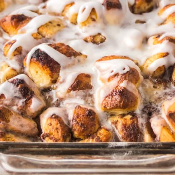 Close-up of a glass baking dish filled with golden-brown cinnamon roll casserole topped with a white icing drizzle.