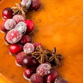 A creamy eggnog flan topped with sugared cranberries and star anise, with a glossy caramel surface.