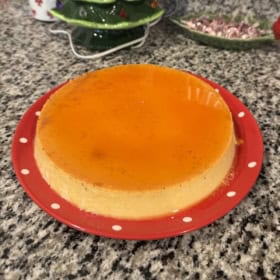 A creamy eggnog flan with glossy caramel top sits on a red plate.