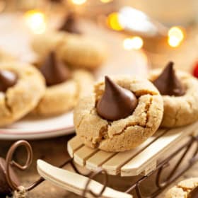 A close-up of soft peanut butter blossom cookies topped with chocolate kisses, one displayed on a small wooden sled.