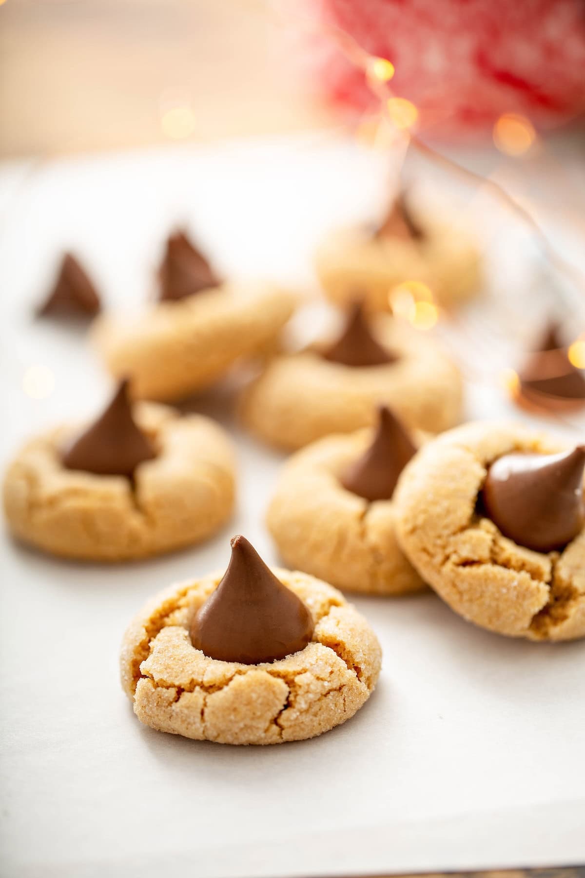 These are the softest Peanut Butter Blossoms you’ll ever make! Perfect for holiday trays, neighbor gifts, or sneaking fresh from the oven. Peanut butter kiss cookies topped with chocolate kisses are arranged on parchment paper.