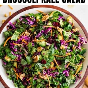 A large wooden bowl filled with chopped broccoli, kale, red cabbage, carrots, walnuts, and dried cranberries, making a colorful, crunchy kale salad.