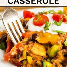 A close-up of a taco Dorito casserole topped with melted cheese, sour cream, chopped tomatoes, and cilantro, with a fork inserted.
