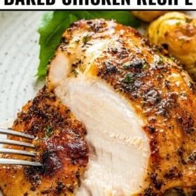 A fork cuts into a juicy, seasoned baked chicken breast with crispy skin, garnished with herbs and served with roasted potatoes on a plate.