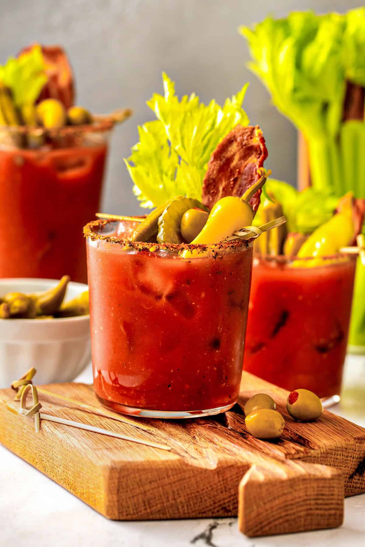 Packed with bold Cajun seasoning, zippy horseradish, and fresh garlic for just the right amount of heat, this is the best Bloody Mary recipe! A homemade Bloody Mary drink garnished with celery, pickles, olives, and bacon sits on a wooden board with another cocktail in the background.