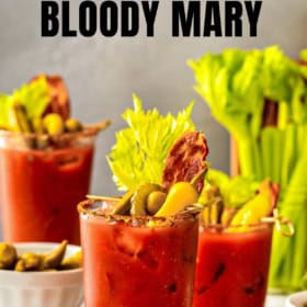 Three of the best Bloody Mary cocktails garnished with celery, olives, pickles, and bacon are displayed on a table, surrounded by fresh ingredients.