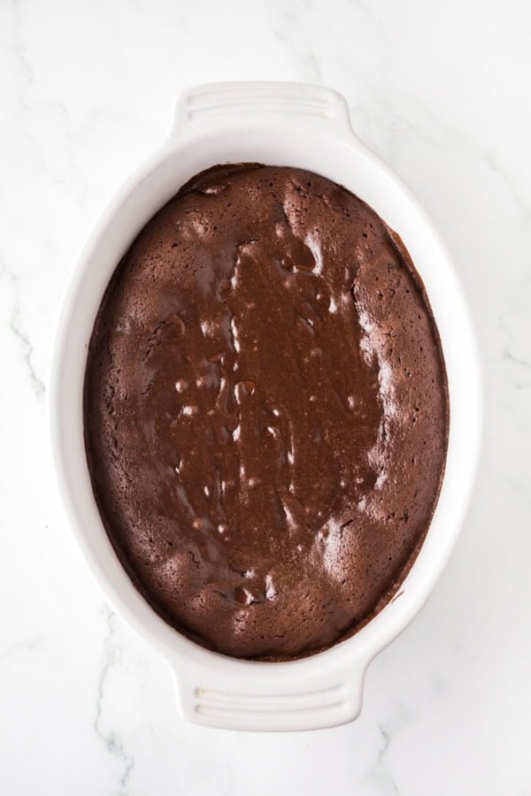 A white oval baking dish filled with freshly baked chocolate pudding cake, with a glossy center and set edges.
