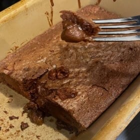 A close-up of a partially eaten chocolate pudding cake in a baking dish, with a fork lifting a gooey bite from the rich and fudgy interior.