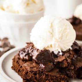 A decadent chocolate pudding cake topped with a scoop of vanilla ice cream sits on a plate. The cake appears gooey and rich, with a melted chocolate pudding filling visible.