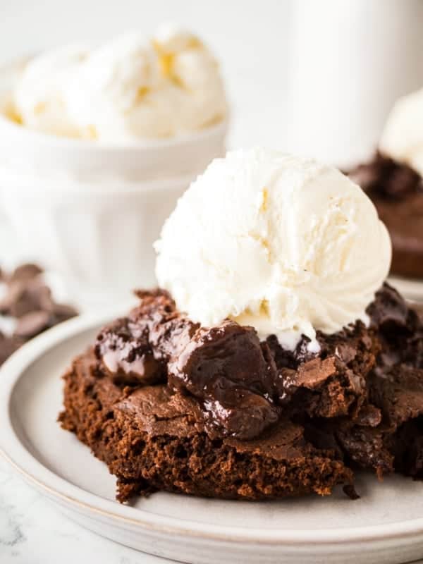 A decadent chocolate pudding cake topped with a scoop of vanilla ice cream sits on a plate. The cake appears gooey and rich, with a melted chocolate pudding filling visible.