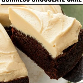 A rich slice of homemade Guinness chocolate cake with creamy Irish cream frosting is being lifted from a round cake.