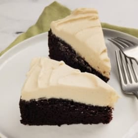 Two slices of chocolate cake with Guinness topped with a creamy Irish cream frosting on a white plate, next to two forks and a green napkin.