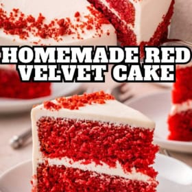A slice of homemade red velvet cake with cream cheese frosting sits on a white plate, in front of the remaining cake.