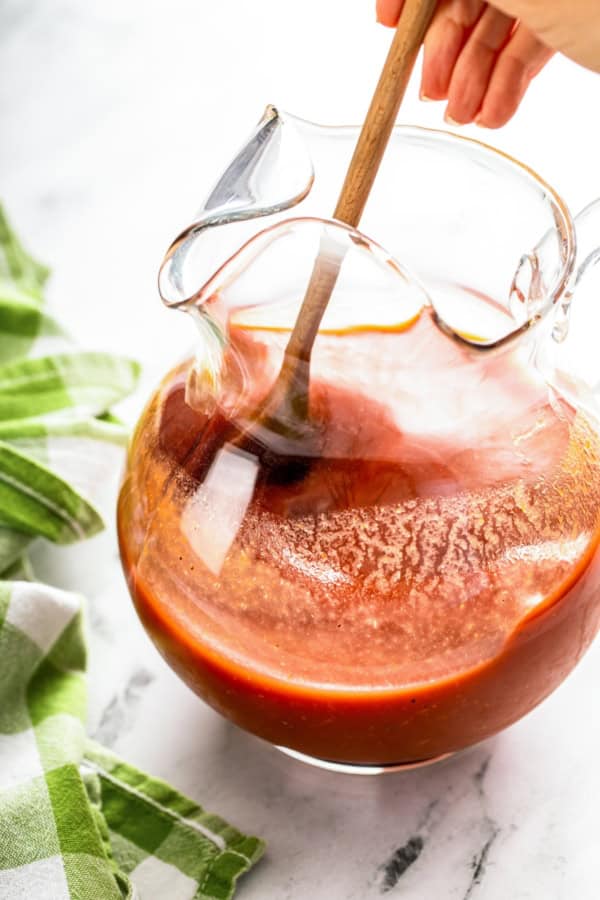 Packed with bold Cajun seasoning, zippy horseradish, and fresh garlic for just the right amount of heat, this is the best Bloody Mary recipe! A wooden spoon stirs together a homemade Bloody Mary mix in a clear glass pitcher on a marble surface.