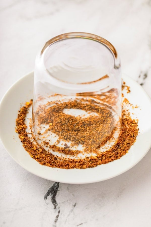 Packed with bold Cajun seasoning, zippy horseradish, and fresh garlic for just the right amount of heat, this is the best Bloody Mary recipe! A glass turned upside down on a white plate, with the rim being coated in cajun seasoning.