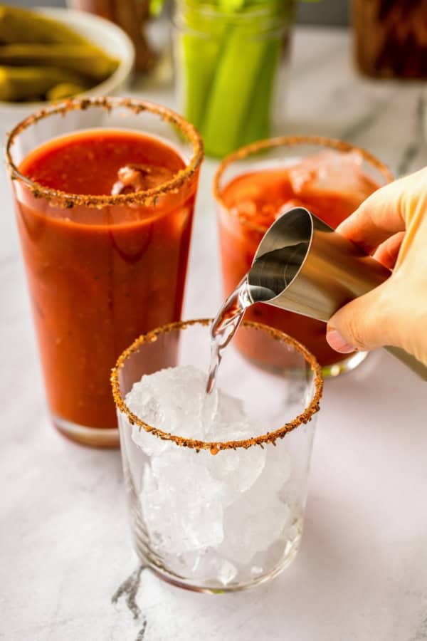 Packed with bold Cajun seasoning, zippy horseradish, and fresh garlic for just the right amount of heat, this is the best Bloody Mary recipe! A hand pours vodka from a metal jigger into a glass filled with ice and a spiced rim.