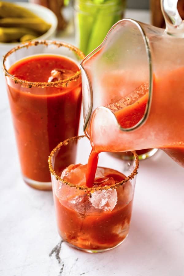 Packed with bold Cajun seasoning, zippy horseradish, and fresh garlic for just the right amount of heat, this is the best Bloody Mary recipe! A pitcher pours homemade Bloody Mary mix into a glass with ice, vodka, and a spiced, seasoned rim.