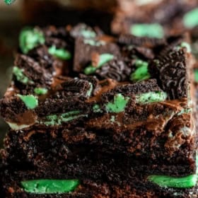 Close-up of two stacked mint brownies topped with crumbled mint Oreo cookies and visible green Andes mint pieces.